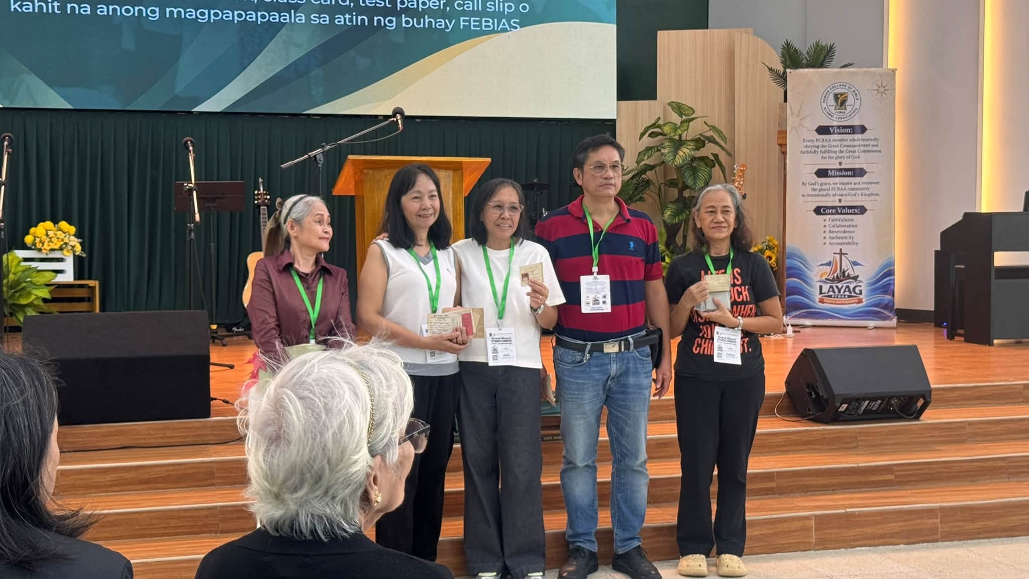 Alumni on stage proudly displaying keepsakes from their FEBIAS days